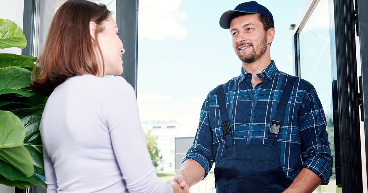 Happy young technician in workwear shaking hand of housewife